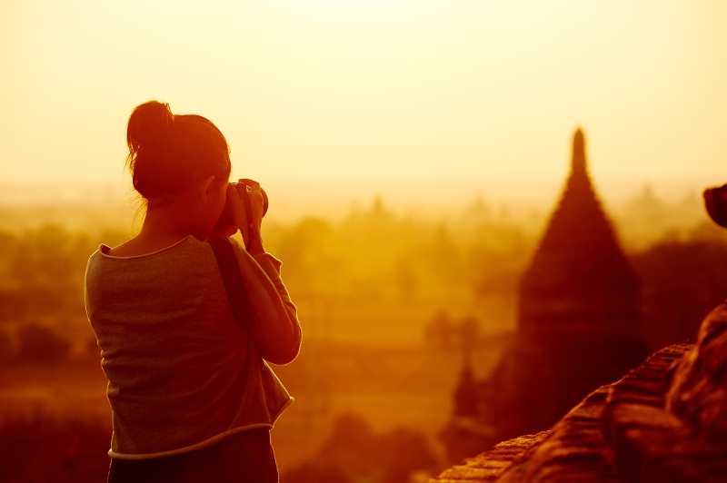 A young woman photographs the temples of Bagan in Myanmar at sunset.