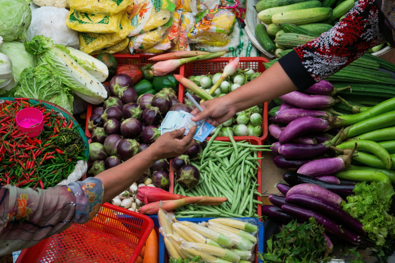birds eye view over colourful vegetables and fruit. two hands exchange money