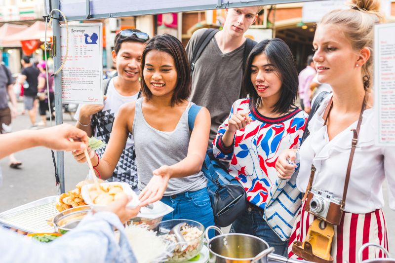 group of people waiting around a market stall for food, smiling