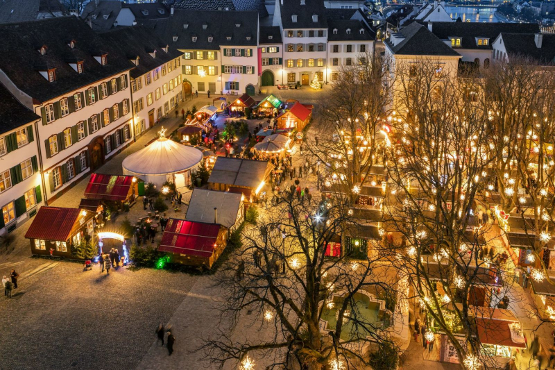 An aerial shot of the basel christmas markets. Big light bulbs are hung from trees 