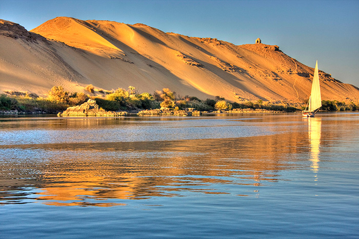 A felucca sails next to sunlit dunes on the River Nile in Egypt - cruise trends to try