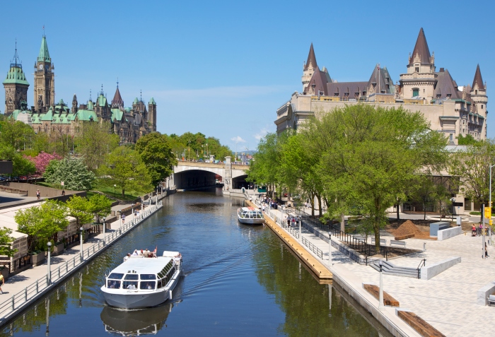 Boats cruise up Rideau Canal next to a park and parliament house - cruise trends to try