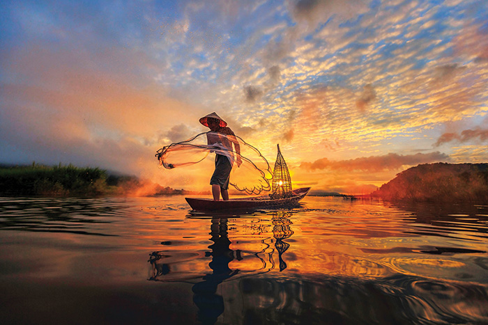 A fisherman casts his net at sunrise on the Mekong River, Vietnam - cruise trends to try