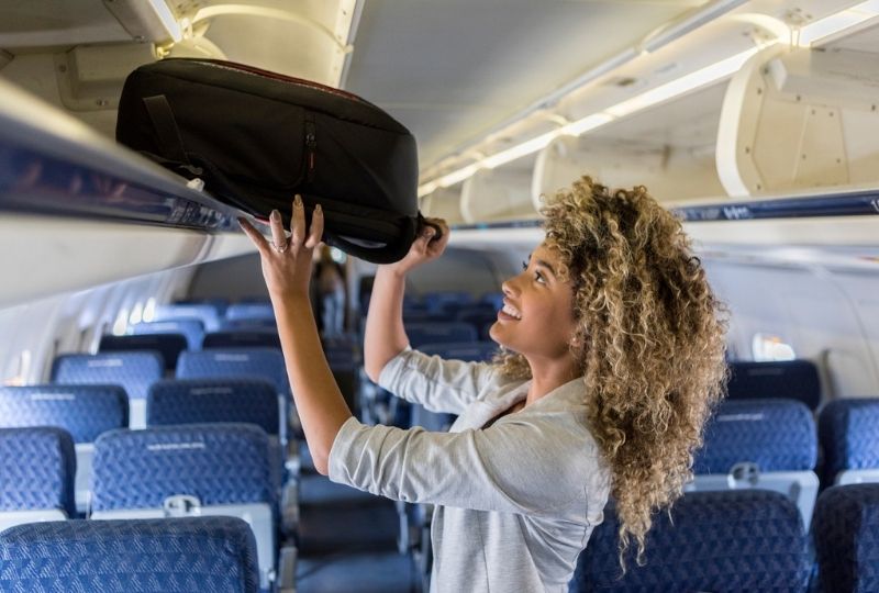 Image of someone placing carry on luggage into overhead compartment