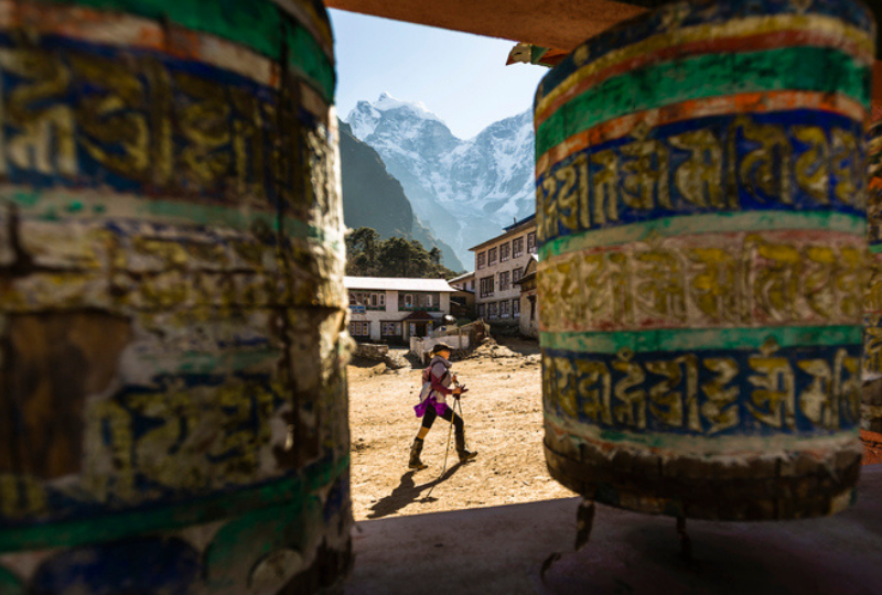 A woman is hiking past prayer wheels at Tengboche Monastery, Nepal