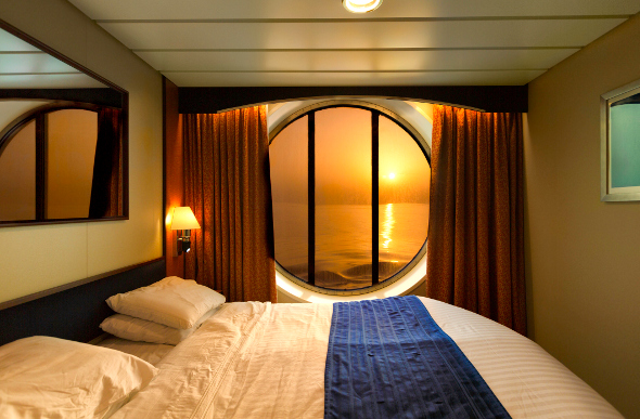 A cruise ship cabin with a window looking out at the ocean