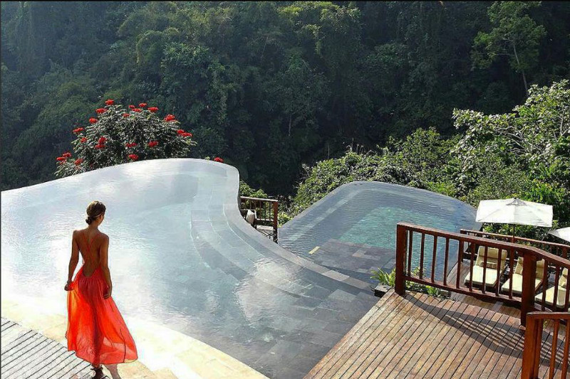 Beautiful lady standing in front of an infinity pool overlooking the jungle in Bali.