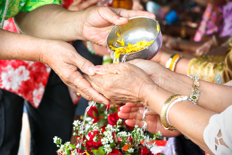 Pouring water infused with flower petals onto hands as part of a Songkran ceremony inside a temple in Thailand.