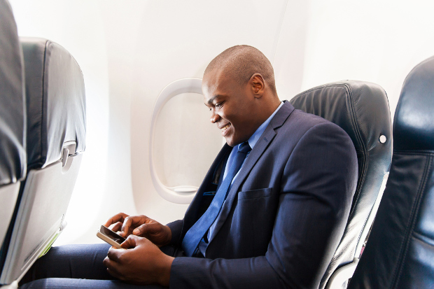 A man sitting in a window seat on an airplane using his phone