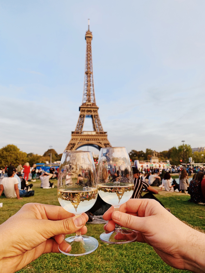 a couple toast champagne glasses in front of the Eiffel Tower in Paris - 14 romantic travel experiences for valentines day