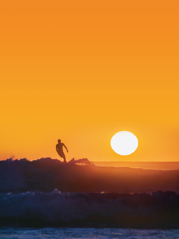 surfer on wave with sun setting behind