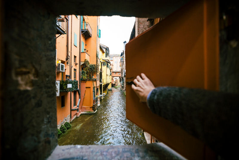 man pushing open window onto canal Bologna italy