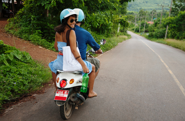 A couple riding a motor scooter through the jungle