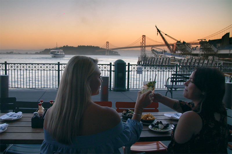 Two women dine at Hog Island Oyster Bar and watch the sun set over the water in San Francisco.