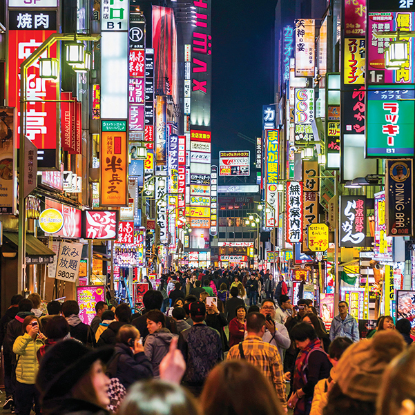 Crowds of commuters fill the streets of neon-lit Shinjuku in Tokyo at night