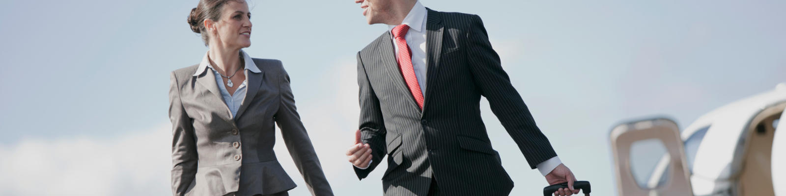 A professionaly dressed man and woman walking together off the tarmac