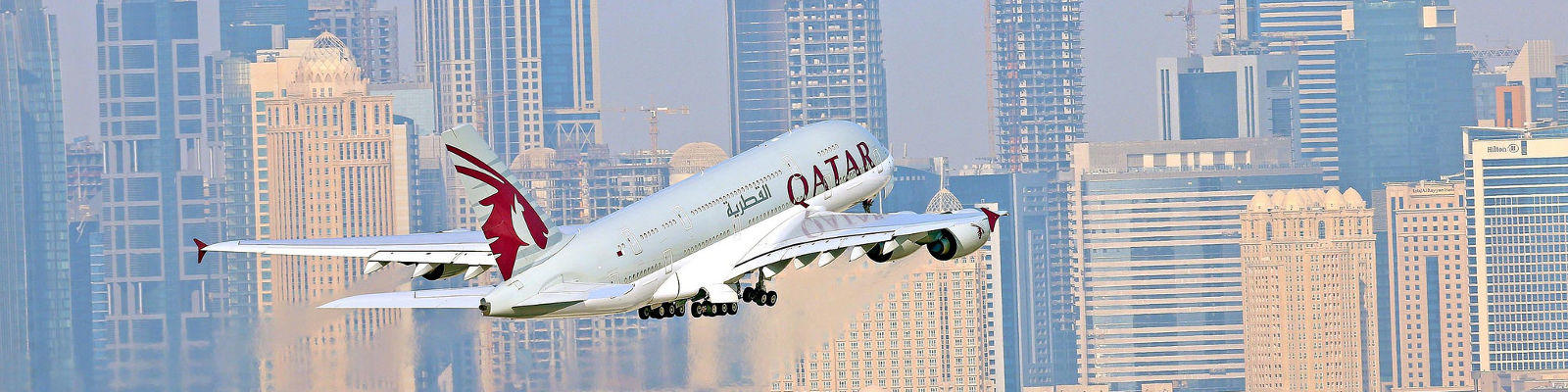 qatar a380 flying with doha skyline behind