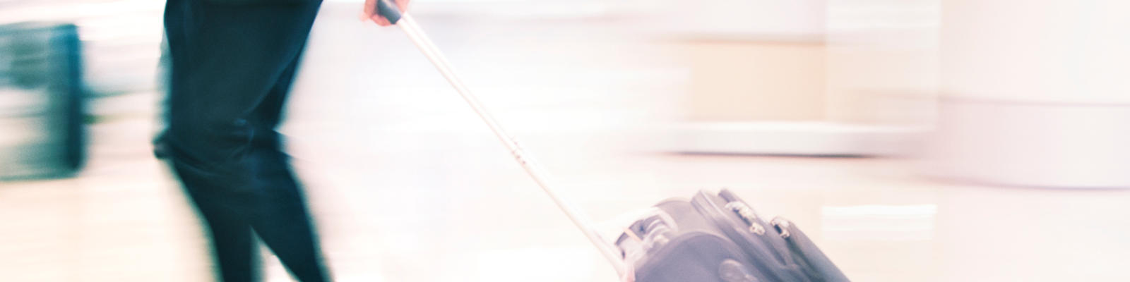 A man rushing through the airport with a carry-on in tow