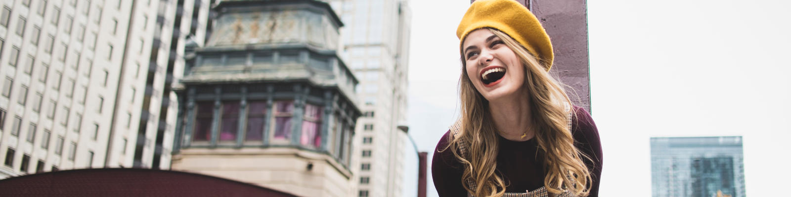 Model outdoors in Chicago laughing. She is wearing a Yellow beanie