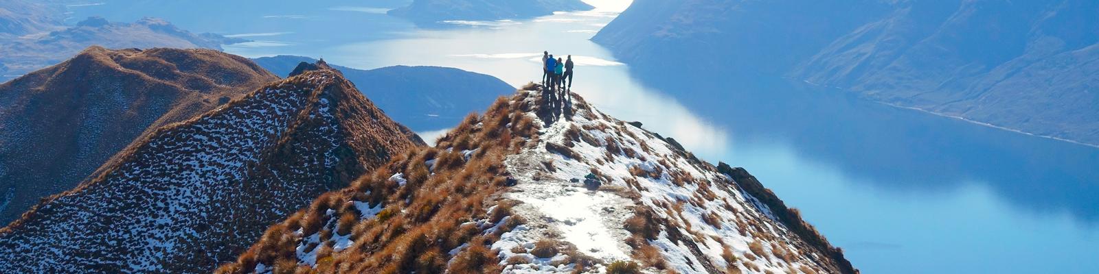 Distant view of hikers standing on a cliff against lake during winter, Queenstown