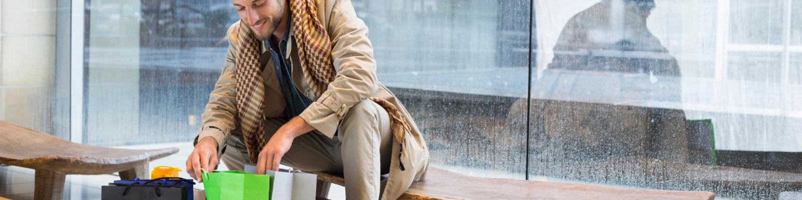 A man happily looking in some shopping bags while sitting on a bench at the airport