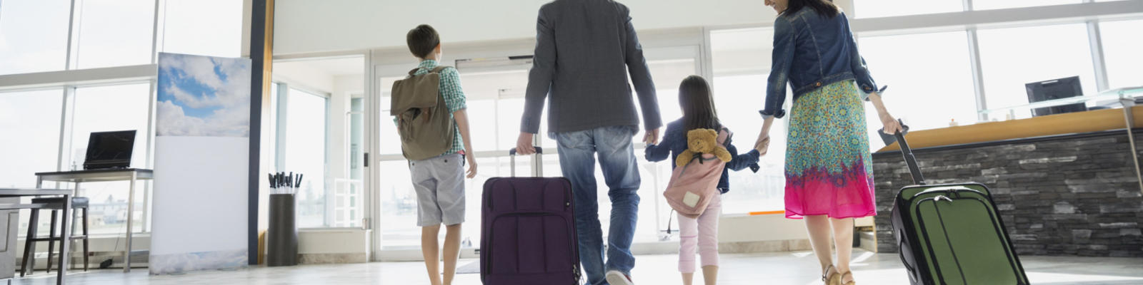 A family of four walking through the airport hand in hand with their bags.