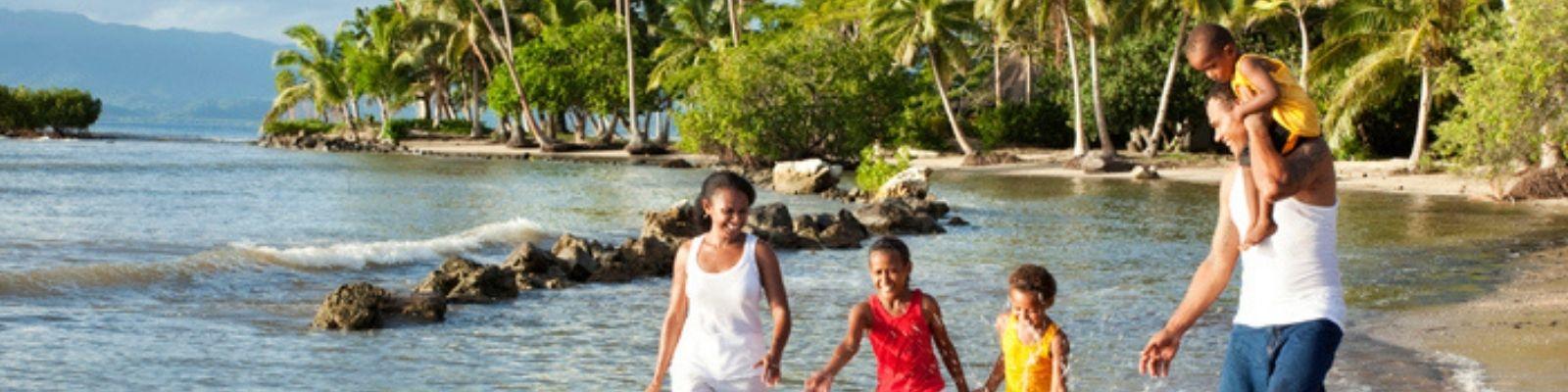 Family plays in shallow water at beach with palm tress in background