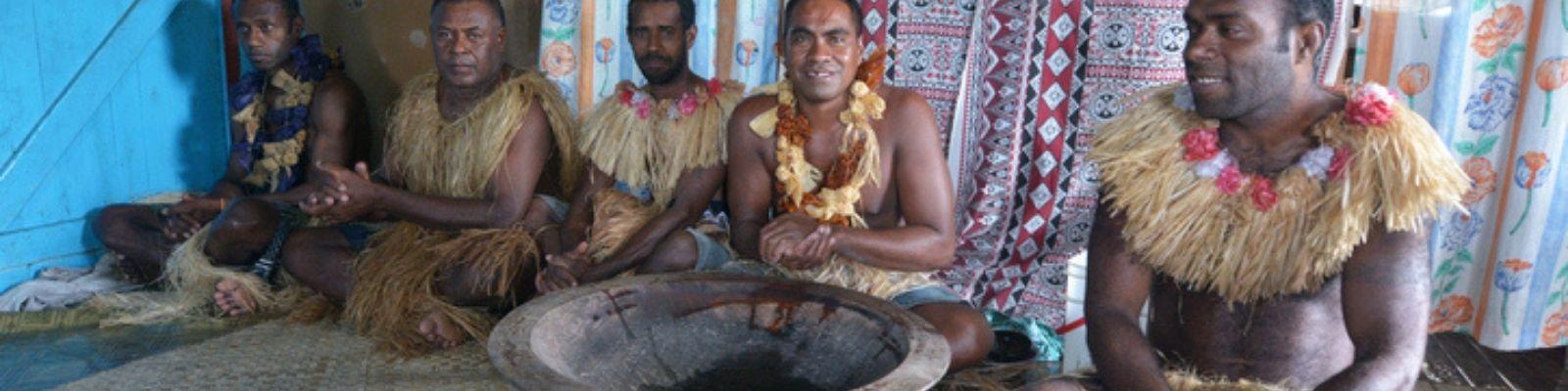 Fijian men sitting on straw mat with bowl of kava in front 