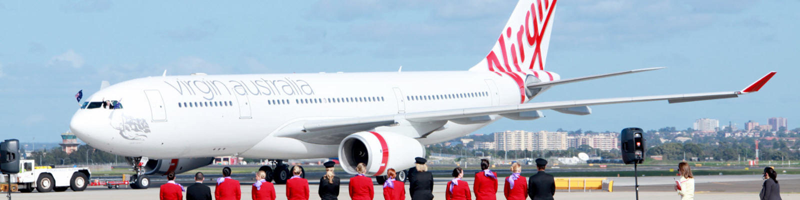 Flight crew standing on a red carpet on the runway looking at a Virgin Australia airplane