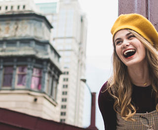 Model outdoors in Chicago laughing. She is wearing a Yellow beanie