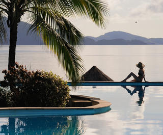 Woman sitting on the edge of the pool at a beachfront resort as the sun goes down at Hamilton Island.