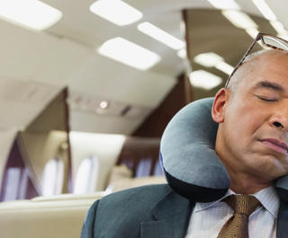 A man sleeping on a plane with a neck pillow around his neck