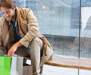 A man happily looking in some shopping bags while sitting on a bench at the airport