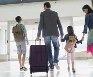 A family of four walking through the airport hand in hand with their bags.