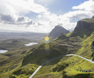 road winding down the side of bare scottish mountain with valley 