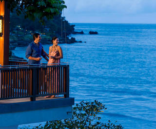 Two people standing on a balcony with drinks overlooking the ocean