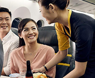 A man and a woman sitting in business class on Scoot, being served some food and drinks