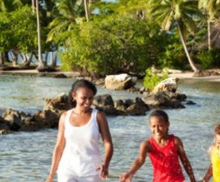 Family plays in shallow water at beach with palm tress in background