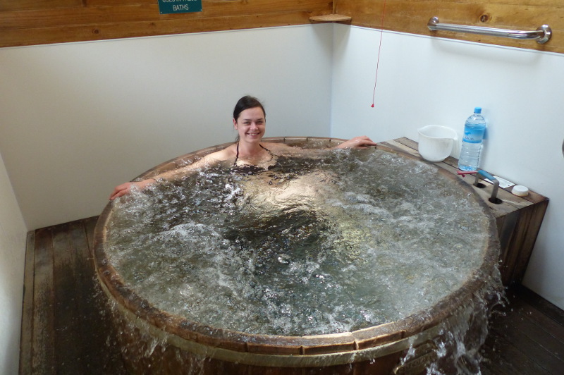 A woman sits in an overflowing round tub full of soda water from natural hot springs.