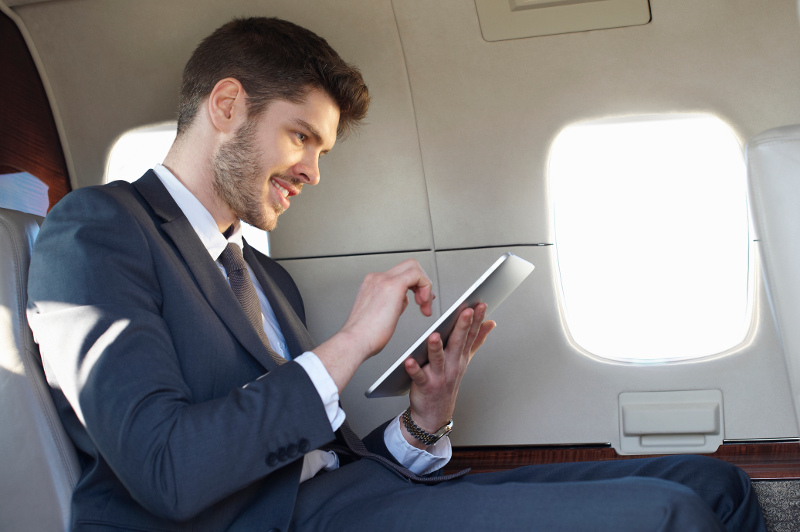 A young businessman uses a tablet on a plane.
