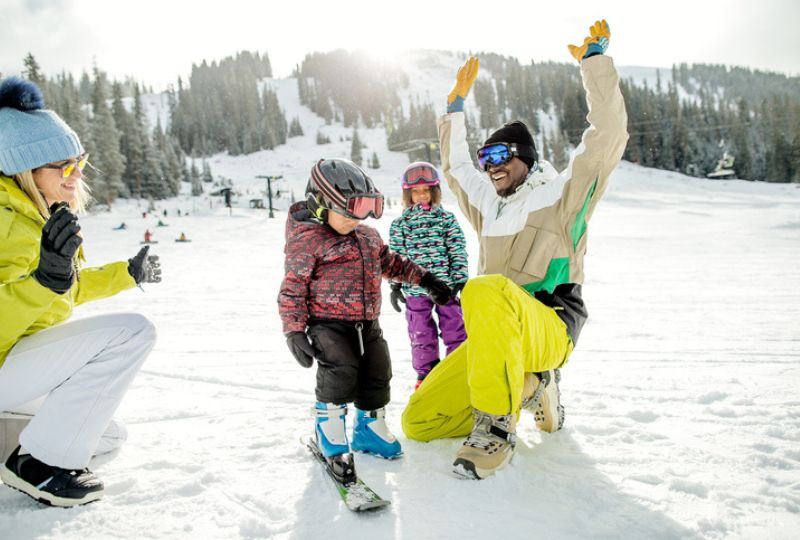 Family with two adults and two children in snow clothes playing in snow